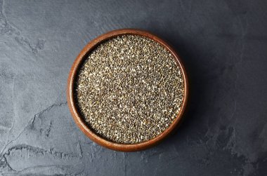 Organik çiğ chia tohumları. Yuvarlak ahşap kasede, koyu taşlı arka planda süper yiyecekler.