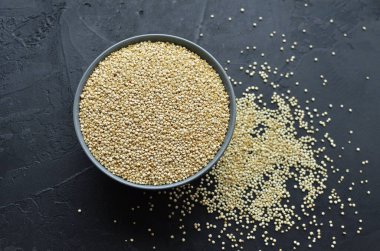 Koyu beton arka planda gri seramik kasede kuru organik kinoa tohumları.