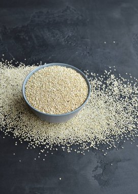 Siyah taş zemin üzerinde seramik tabakta beyaz kinoa tohumları.