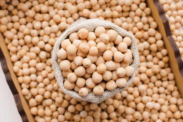 Dry organic uncooked chickpeas in wooden box and sack, top view. — Stock Photo, Image