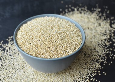 Bowl with white uncooked quinoa seeds superfood on dark concrete background