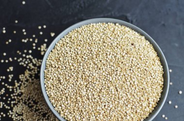 Koyu beton arka planda gri seramik kasede kuru organik kinoa tohumları.