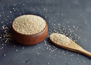 Organic dry quinoa grains in wooden bowl and spoon on black stone background