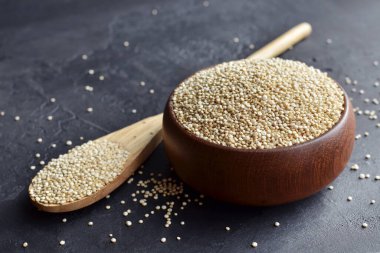 Organic dry quinoa grains in wooden bowl on black stone background