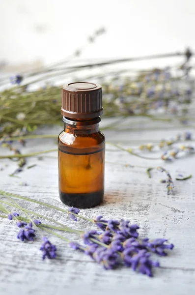 Dark glass bottle with essential lavender oil and fresh lavender flowers over vintage wooden background — Stock Photo, Image