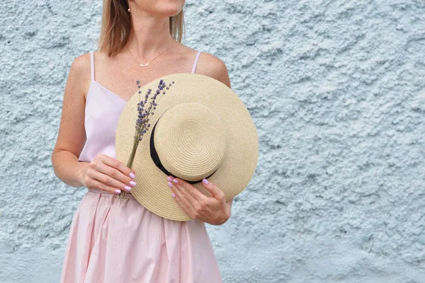 Bouquet of dry natural lavender flowers and summer straw hat in womens hands, against concrete wall background, copy space. — Stock Photo, Image