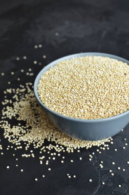 Dry quinoa seed grain in ceramic plate over black grange background