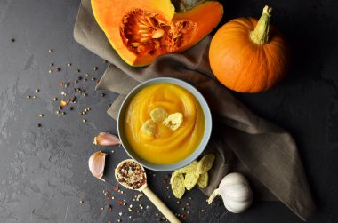 Buğday buğdaylı kabak çorbası ve taze balkabağı, sarımsak ve baharatlar keten örtüde koyu grunge arka planda. Sonbahar mevsimi konsepti. Üst görünüm