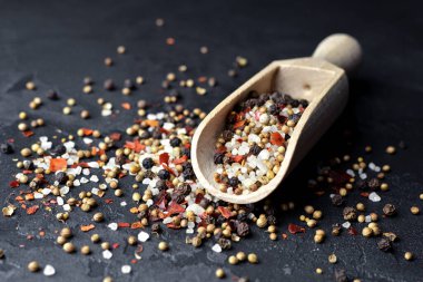 Koyu arka planda ahşap kepçe içinde çok renkli baharatlar - biber, tuz, kardamon, hardal tohumu ve kırmızı biber taneleri. Yiyecek malzemeleri..