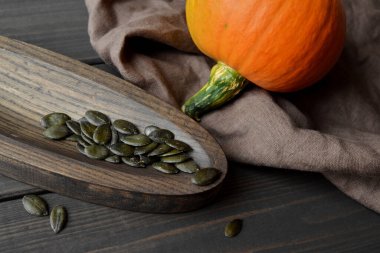 Raw organic green pumpkin seeds in wooden plate with pumpkin on wooden dark background with flax napkin