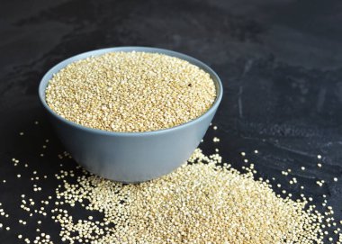 Dry quinoa seed grain in ceramic plate over black grange background