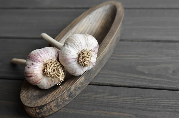 Dry fresh organic garlic bulbs on wooden plate over dark wooden background — Stock Photo, Image