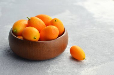 Çiğ organik kumkuat narenciye meyveleri ahşap kasede beton arka planda. Sağlıklı vejetaryen yemekleri. Boşluğu kopyala.