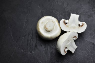 Karanlık arka planda taze şampiyon mantarları, dilimlenmiş ve tek parça, pişirmeye hazır. Üst görünüm, alanı kopyala.