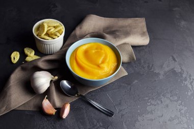 Kabak ezmesi çorbası, kıtır ekmek ve seramik kasede taze sarımsak, siyah kaşık ve keten peçeteli.