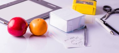 Office desk with pens, clock, note paper and tablet. Office supplies on a white background.