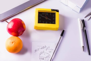 Office desk with pens, clock, note paper and tablet. Office supplies on a white background.
