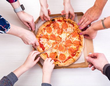 Everyone loves pizza. Close-up top view of young people choosing slices of pizza during lunch indoors.