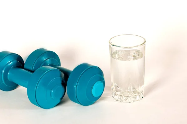 A glass of water and dumbbells for sports. The concept of sports and fasting.