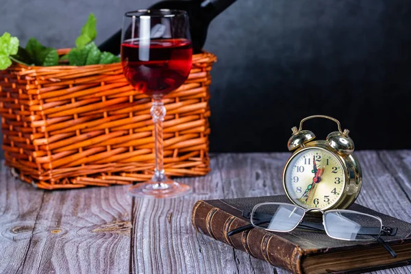 A bottle of wine in the basket, a glass of wine and a book. Glasses and alarm clock. The concept of home recreation. Self-isolation of the house.