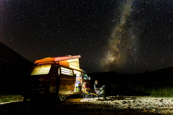Young couple in a vintage van staring at the milkyway during a roadtrip