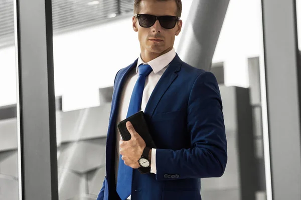 Un hombre con traje azul y gafas en un edificio moderno —  Fotos de Stock