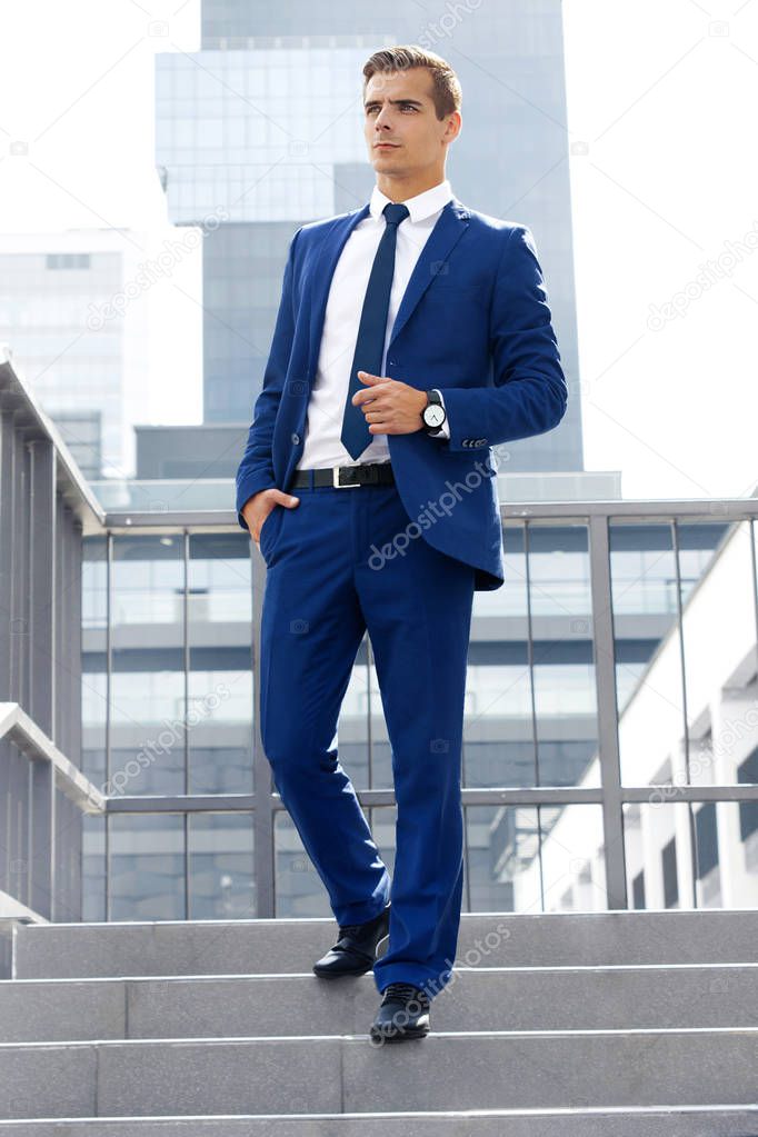 Handsome man in a blue suit against a city background on a sunny day