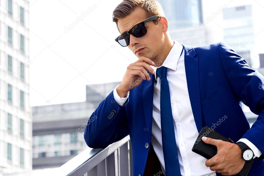 Handsome man in a blue suit against a city background on a sunny day