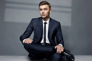 Bir adam bir ceket ve kravat kameraya bakarak oturuyor