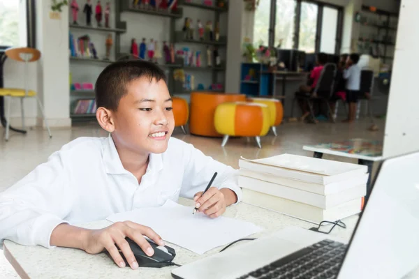 亚洲男孩微笑着做他的家庭作业在图书馆 他很高兴 图库图片