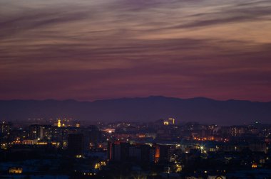 Kızıl günbatımı gökyüzü şehrin ve dağların üzerinde