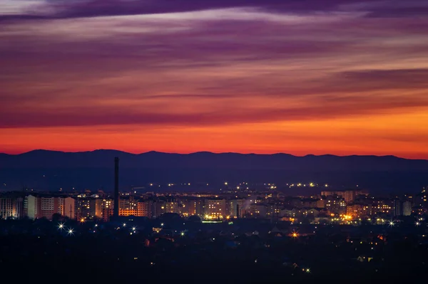 Röd solnedgång himmel över staden och bergen silhuett — Stockfoto