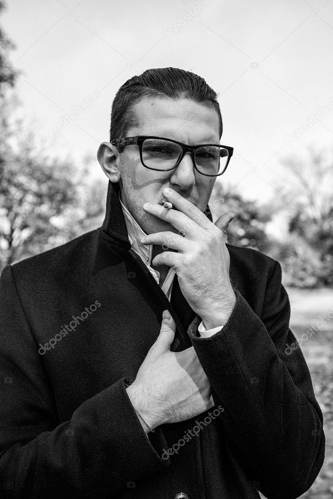 sexy man in a black coat smokes on the street