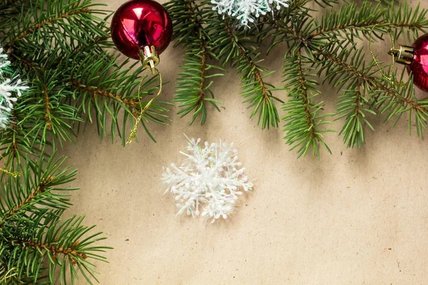 Çam dalları üzerinde kırmızı topları ve rustik bej renkli arka plan üzerinde kar taneleri ile şenlikli Noel sınır