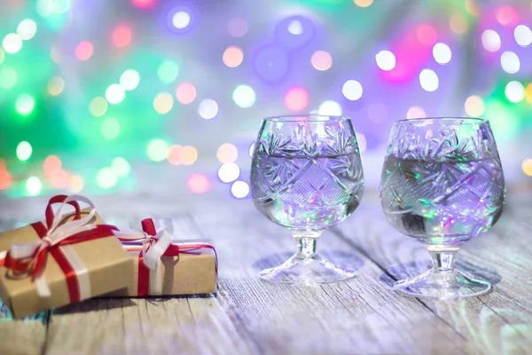 Stillleben mit zwei Gläsern Sekt und Geschenkschachteln mit bunten Lichtern im Rücken. — Stockfoto