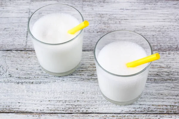 Glasses of milk with yellow straws on white wooden background