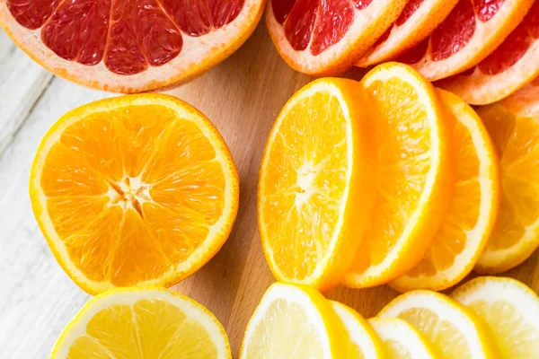 In Scheiben geschnittene frische Zitronen, Grapefruits, Orangen auf einem Holzschneidebrett mit einem Messer — Stockfoto