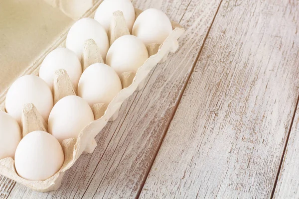 Cardboard egg rack with eggs on white wooden table, toned