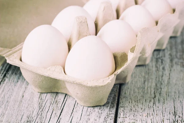 Cardboard egg rack with eggs on white wooden table, toned