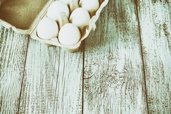 Cardboard egg rack with eggs on white wooden table, toned