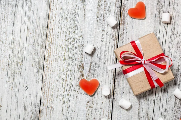 Valentines Day candy hearts marshmallows and box of gifts in craft paper over white wooden background