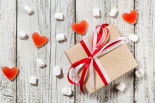 Valentines Day candy hearts marshmallows and box of gifts in craft paper over white wooden background.