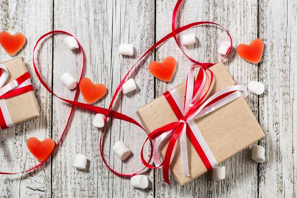 Valentines Day candy hearts marshmallows and box of gifts in craft paper over white wooden background.