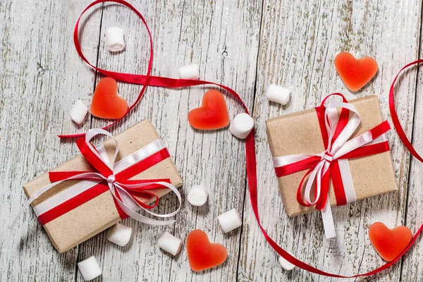 Valentines Day candy hearts marshmallows and box of gifts in craft paper over white wooden background.