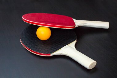 İki Masa Tenisi veya ping pong raketleri ve siyah bir arka plan üzerinde topu