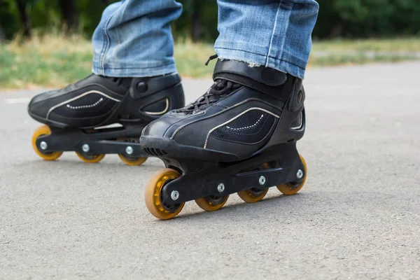 Giovane in jeans blu che cavalca pattini a rotelle in città. Chiudi le gambe — Foto Stock