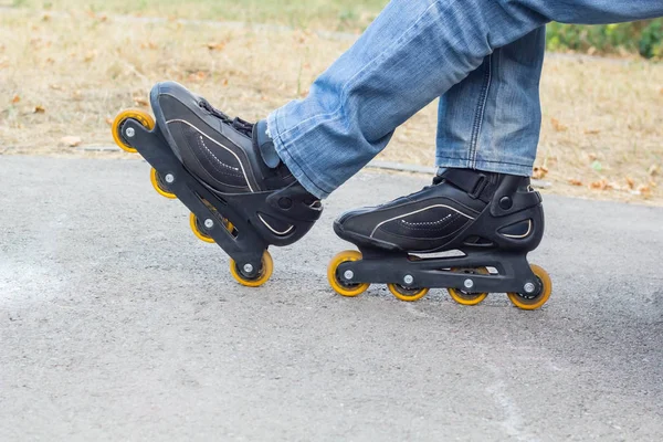 Jeune homme en jeans bleus chevauchant des patins à roulettes dans la ville. Fermer les jambes — Photo