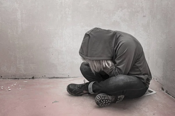 Foto van wanhopige jonge drugsverslaafde dragen kap en zitten alleen in hoek — Stockfoto