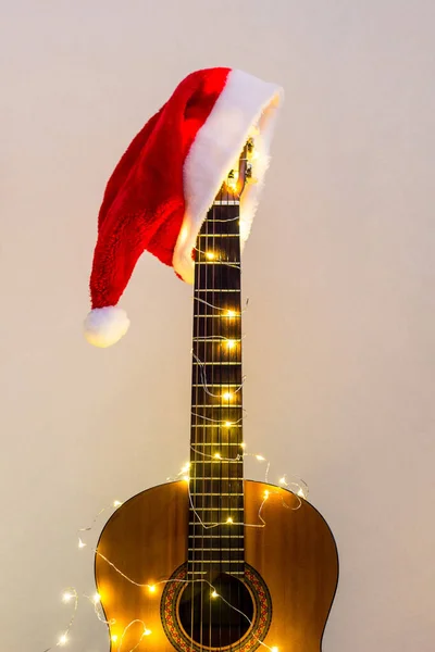 Kırmızı Noel Baba şapkası ve açık renk çelengi olan akustik gitar. Telif alanı ile Noel müziği konsepti