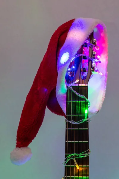 Akoestische gitaar met rode Santa hoed en lichte kleurrijke slinger. Kerstmuziek concept — Stockfoto